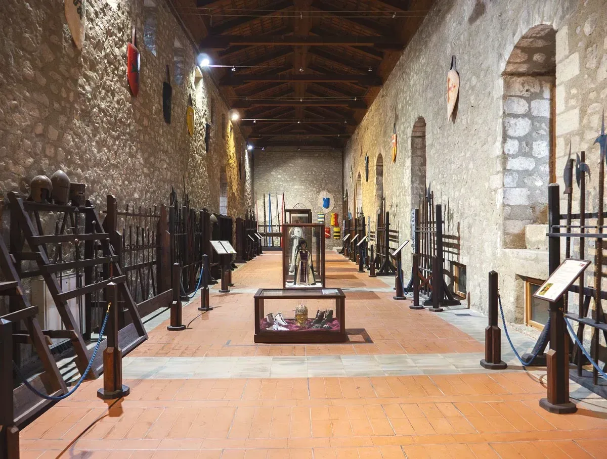 La sala delle armi nel castello, con armature e armi medievali lungo le pareti di pietra